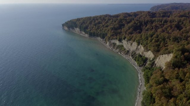 Beautiful landscape colorful forest on cliff at sea shore aerial view. Smoth water surface of transparent sea water on cliff coast and forest in mountain landscape drone view