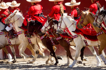 Group of mexican escaramuza girls with red mexican dresses and sombrero ride horseback on a rodeo