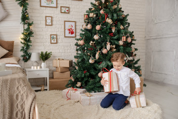 a 6-year blond boy with a present in his hand near a christmas tree and a bed