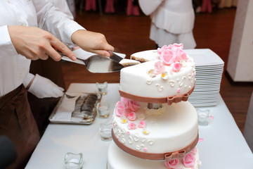 Dłonie kelnerek krojących tort na uroczystości weselnej.