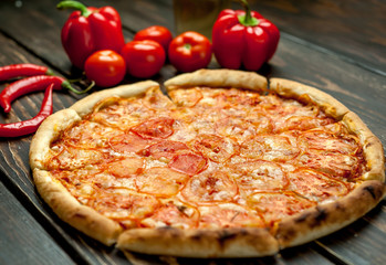 pizza on a wooden table with ingredients, tomato, pepper, sunflower oil