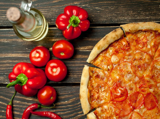 pizza on a wooden table with ingredients, tomato, pepper, sunflower oil