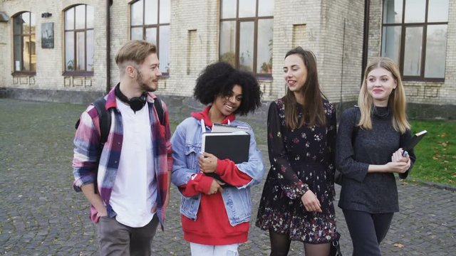Happy International Students talking while walking at the College Campus in front of the University building and smiling.