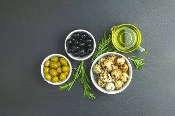 Fototapeten Set of black and green olives, quail eggs on plates, olive oil and rosemary © Victoria Kondysenko
