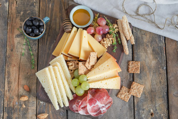 Different kinds of cheese with wine, figs, walnuts, ham, grapes, honey, toast. In a rustic style.