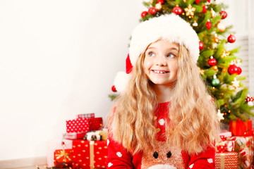 Portrait of cute happy nine year old girl wearing red christmas sweater with many presents, Decorated Christmas tree with stack of wrapped gifts on background. Close up, copy space.