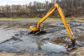 Yellow excavator while working in the mud