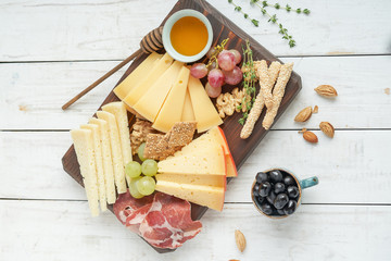 Different kinds of cheese with wine, figs, walnuts, ham, grapes, honey, toast. In a rustic style.