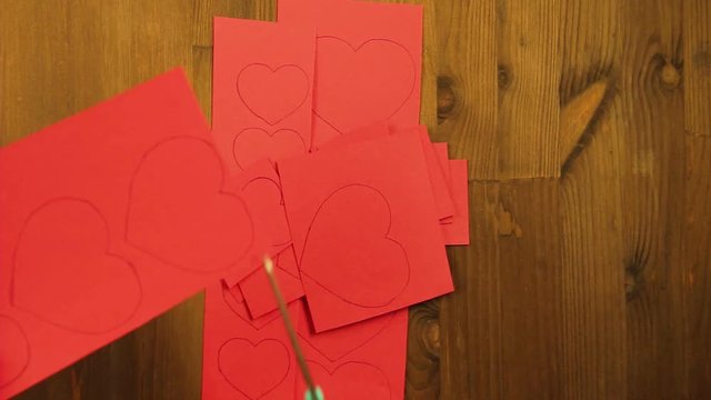 The girl cuts blanks of hearts from red cardboard.