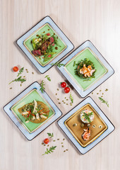 Salads with meat, chicken and fish in white square plates on light wooden table in a restaurant. Healthy food