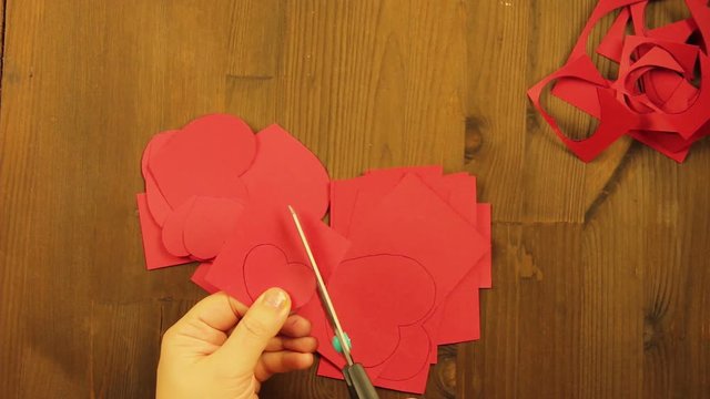 The girl cuts hearts from red cardboard