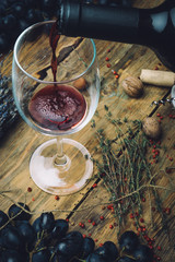 Wine glass with red wine (bio wine), grapes, nuts and herbs on wooden background of an old wooden table.