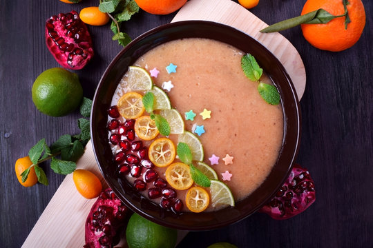 Smoothie bowl garnished with kumquats, pomegranate, lime, mint and sugar sprinkles