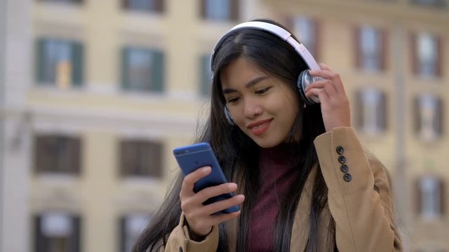 Asian attractive woman in the street,listening music with headphones,smartphone