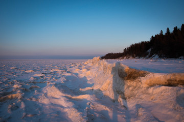Areal view of the frozen sea from the high sandy coast in cold winter day at sunset.