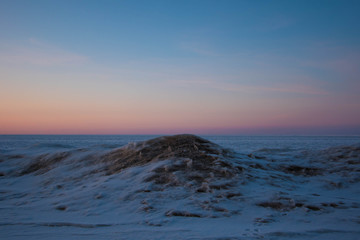 Snowy and frozen open seascape in cold winter weather during sunset.