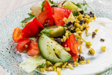Salad with red tomatoes, cucumbers and olives in glass plate on light table in a restaurant. Healthy food