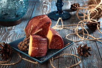 Home-made cheese cut into pieces, on a blue wooden background. Fir cones and a glass of wine. The concept of a home cheese factory.
