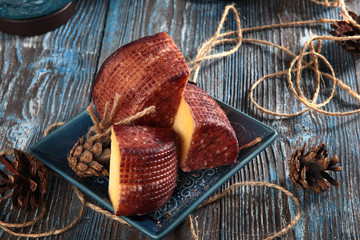 Home-made cheese cut into pieces, on a blue wooden background. Fir cones and a glass of wine. The...