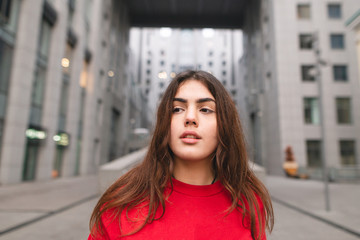 Fototapeta premium Close up portrait of an attractive girl on the background of modern urban architecture. Girl against the backdrop of a city landscape, looking away.