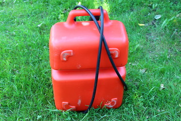 Red portable plastic fuel tank with handle and tube for outboard motor in summer on green grass - motor boat trip