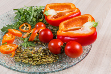 Red pepper with tomatoes cherry and seeds in glass plate n light wooden table. Ingredients in plate