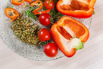 Red pepper with tomatoes cherry and seeds in glass plate n light wooden table. Ingredients in plate