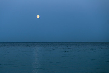 Big full moon is rising above the sea at dusk.