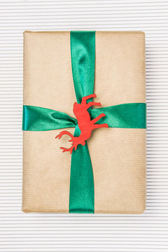 Gift in craft paper with green ribbon and wooden stencil of deera on the light background.