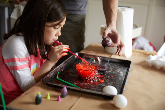 Girl blows soap bubbles to dye easter eggs with, father helps