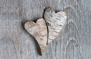 Two hearts of made of birch bark nestle against each other on a rustic wood backround with copy...