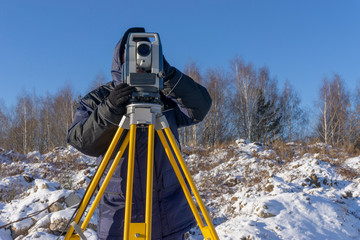 Topographer makes geodetic survey of the construction site for the inventory in winter