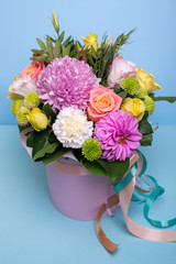 beautiful floral arrangement in the box, pink and yellow rose, pink eustoma, green and pink chrysanthemum, white carnation, pink dahlia on a blue, turquoise background with space for text