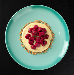 Beet gnocchi, cheese sause and baru nuts on a green plate over black background