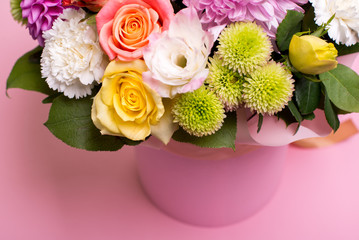 beautiful floral arrangement in the box, pink and yellow rose, pink eustoma, green and pink chrysanthemum, white carnation, pink dahlia on pink background with space for text.