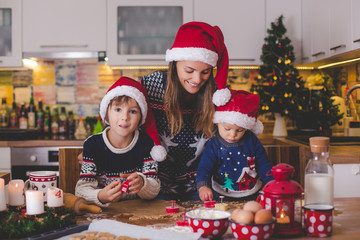 Sweet toddler child and his older brother, boys, helping mommy preparing Christmas cookies at home