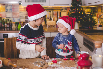 Sweet toddler child and his older brother, boys, helping mommy preparing Christmas cookies at home
