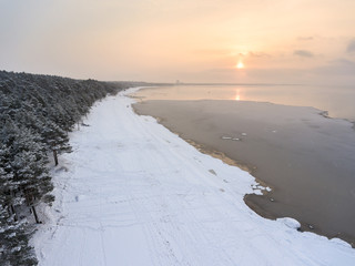 Winter day with low sun and strong frost. Sandy sea beach under snow with ice of water. Aerial view
