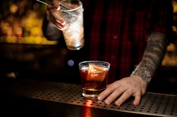 Bartender holding a glass of a Godfather cocktail and a measuring cup