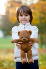 Cute preschool child, boy, holding little brown teddy bear in the park