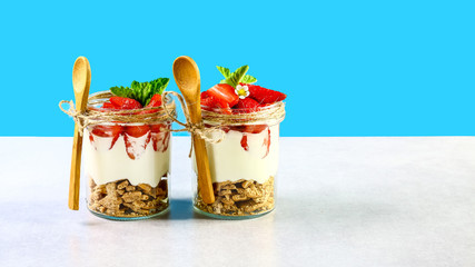 two strawberry yogurt in glass jars, fresh berries in glasses. strawberry, cream cheese healthy breakfast isolated on a blue background. Copy space