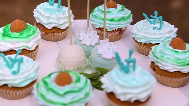 Tasty cupcakes with colourful white and green cream standing on white table outdoors. Sweet cute food for birthday or wedding party. Real time hd video footage.
