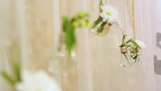 Wedding unusual floral decoration inside of transparent glass mini vases. Small cute bouquets of white fresh flowers hanging from ceiling isolated on fabric background. Details of wedding photobooth.