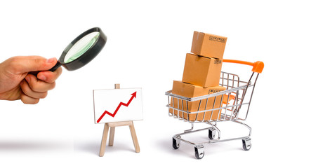 Magnifying glass is looking at the Supermarket cart with boxes and a graph with red arrow, merchandise. selling goods, services, internet commerce, online shopping, trade and turnover. Import, export