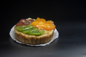fruit tart stacked high with kiwi peach grape dark background.