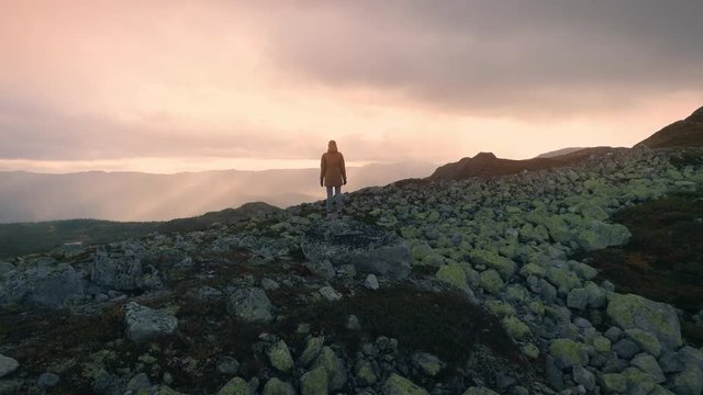 Woman standing on rock on top of the high mountain looking epic view in Norway at sunset aerial shot