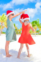 Obraz premium Little adorable girls in Santa hats during beach vacation have fun together