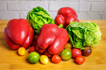 Red peppers, green salad and cherry tomatoes in front of white brick wall