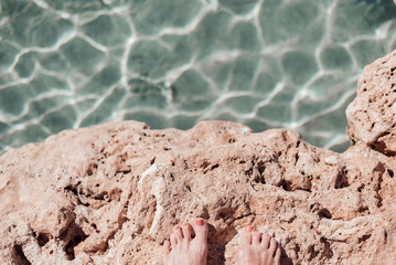 Woman's feet with red manicure above blue sea surface.