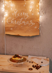 Christmas poster on the wall with garland. Christmas cake on the table.